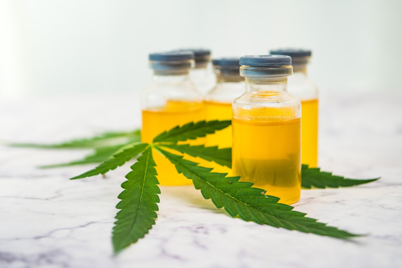 Cannabis oil in the vials with green leaves on marble table. Alt